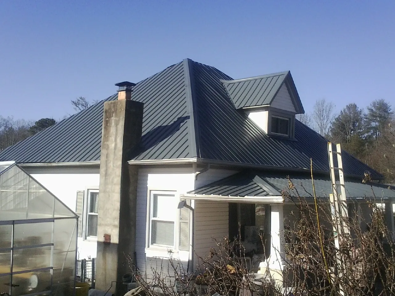 Dark blue standing seam metal roof on a white farmhouse with dormer — Slate & Tile Roof Repair by Roofing Brothers in Placentia
