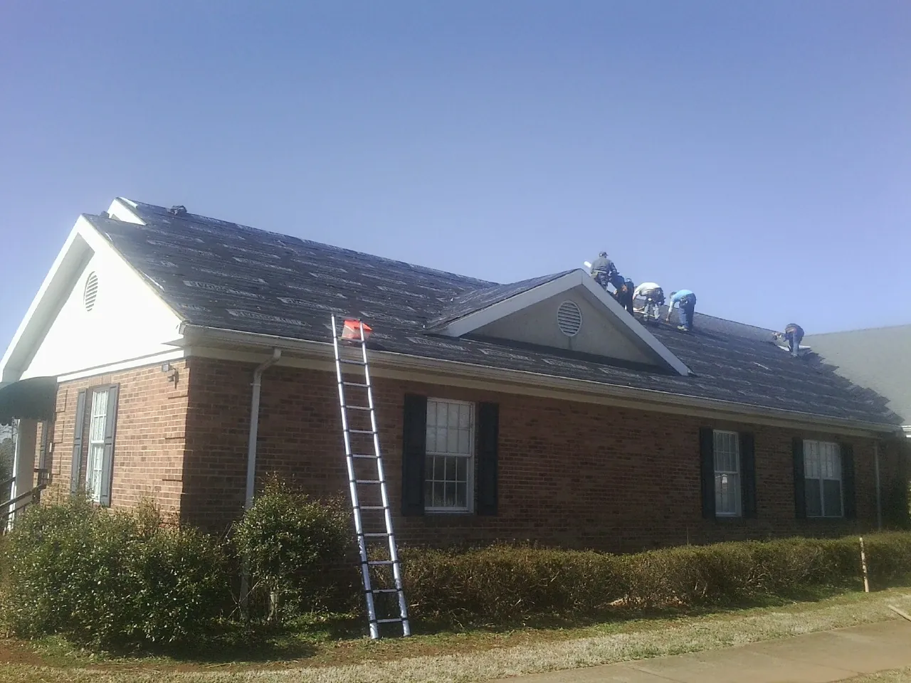 Crew tearing shingles off a brick ranch roof with a ladder set — Emergency Roof Repair work by our crew in Placentia