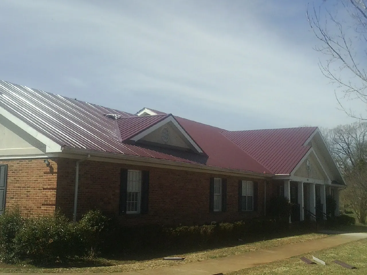 Red metal roof with gabled entries on a long brick building, from a Hail Damage Roof Repair job in Placentia