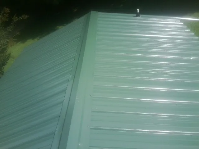 New green metal panels meeting at the ridge of a roof — Flat Roof Repair work by our crew in Placentia